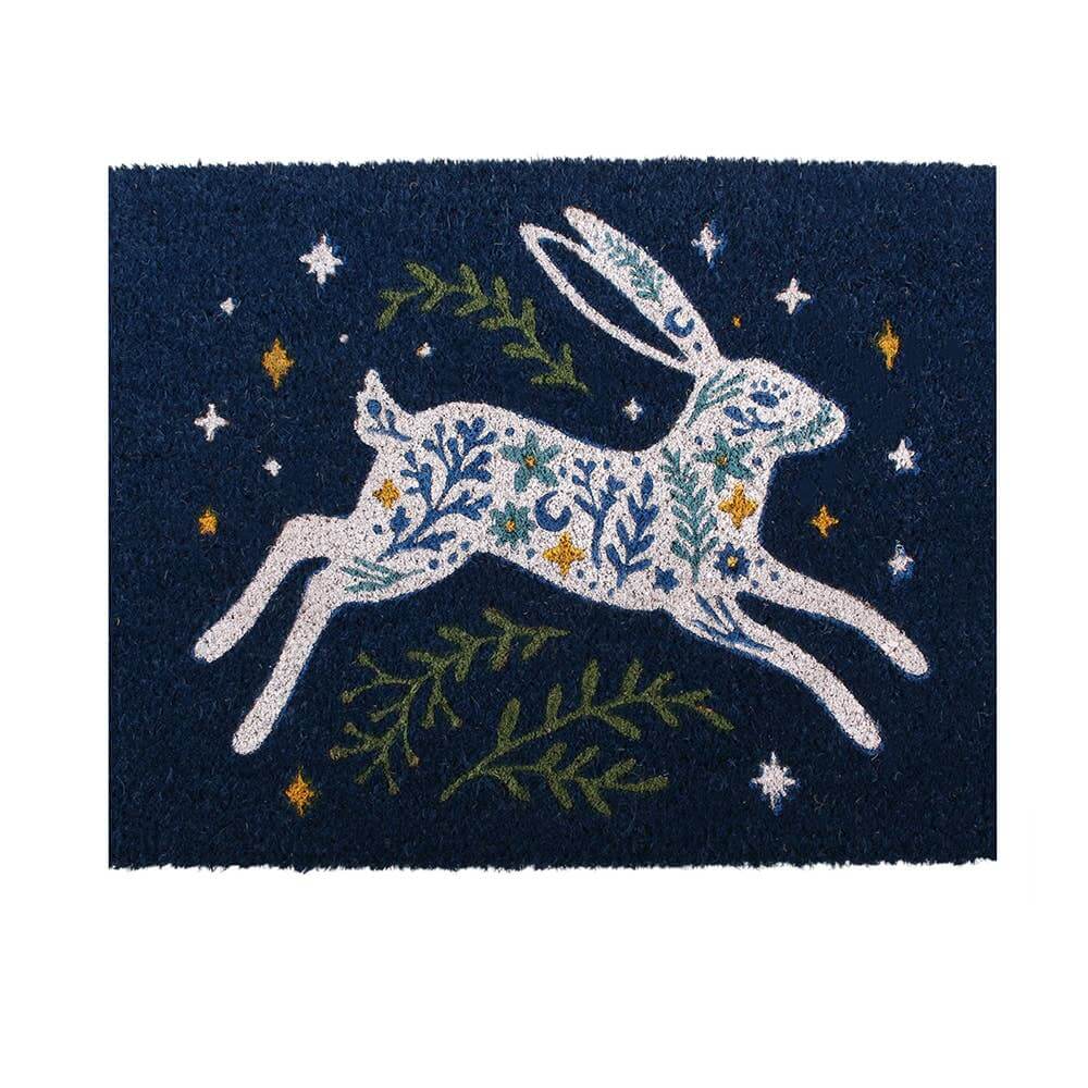 A rectangular dark navy doormat featuring a white hare filled with blue and green floral patterns, surrounded by green leaves and small yellow stars.
