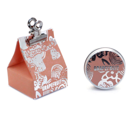 A lip balm called Agnes + Cat in Grapefruit flavor, with a unique packaging design and a metallic clasp.