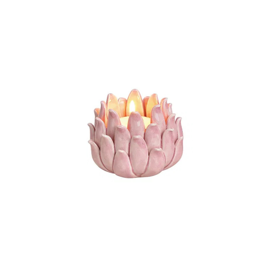 Pink ceramic candle holder with a lit candle on a white background