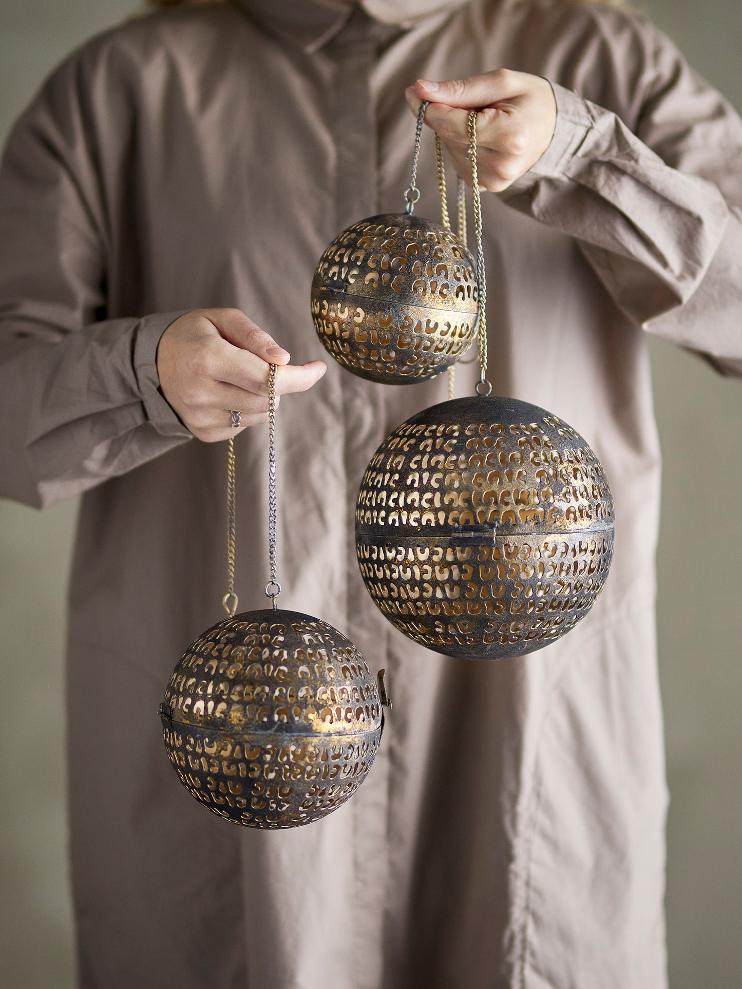 Person holding three decorative spherical objects with intricate patterns against a neutral background