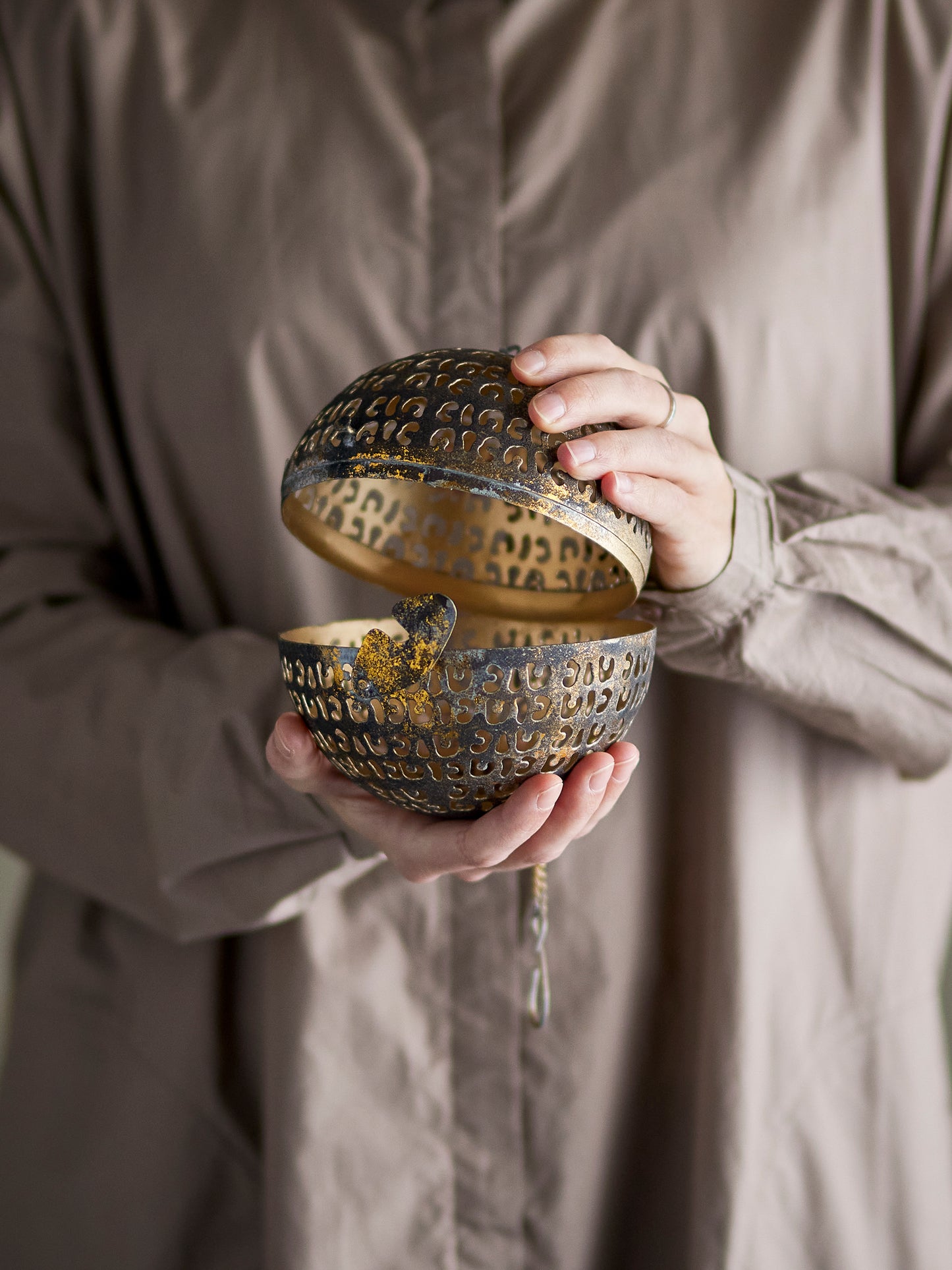 Person holding an ornate, textured metal box with a neutral background