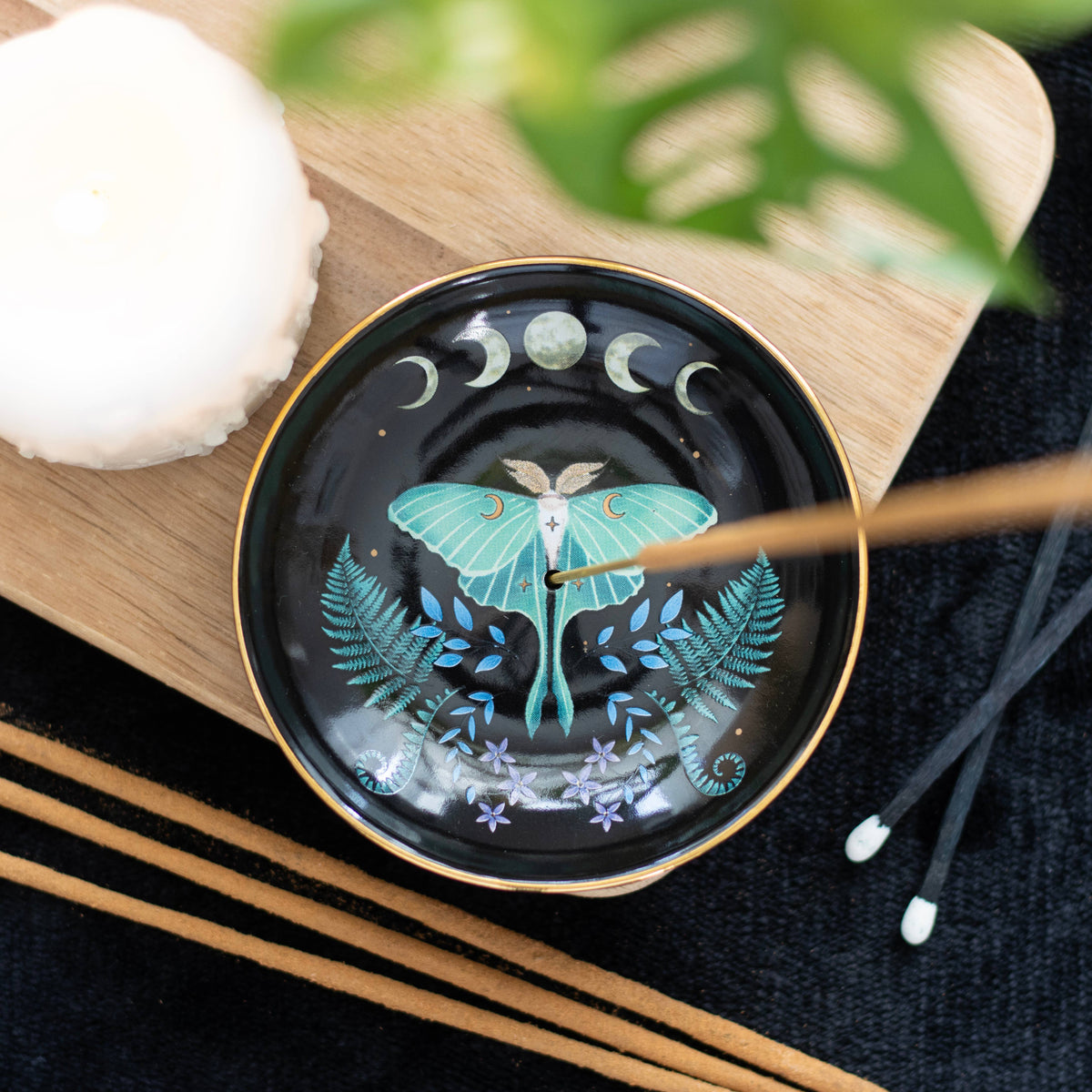 Decorative incense dish with butterfly design on a wooden surface with incense sticks.