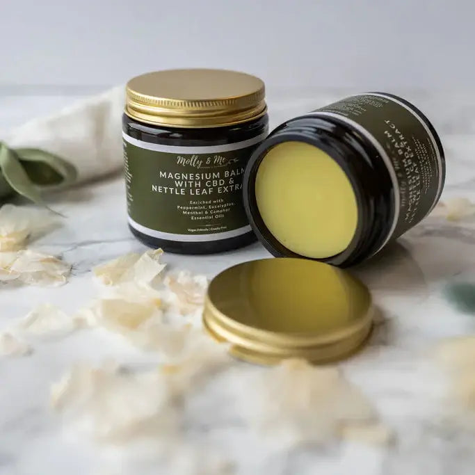Two jars of Molly & Me magnesium balm on a marble surface with leaves and flowers.