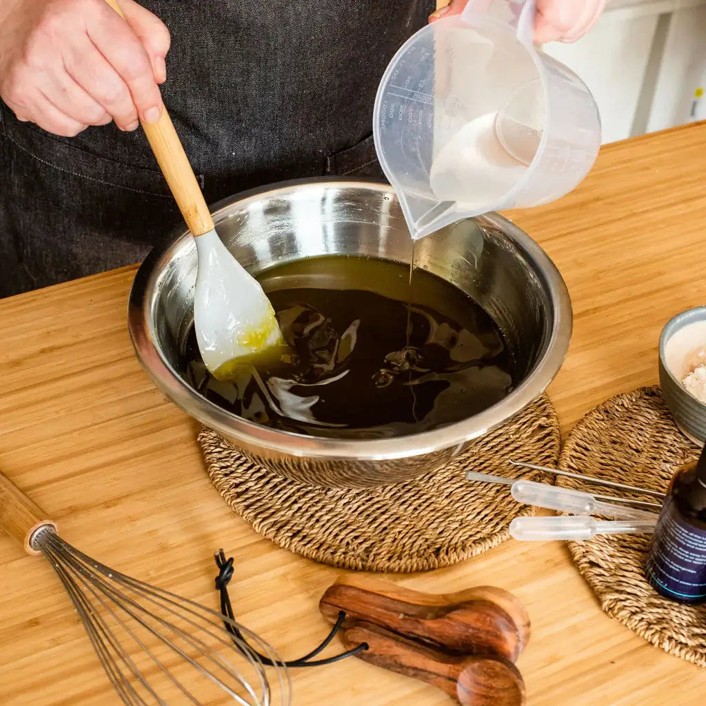 Person pouring liquid into a bowl with a spatula on a wooden table