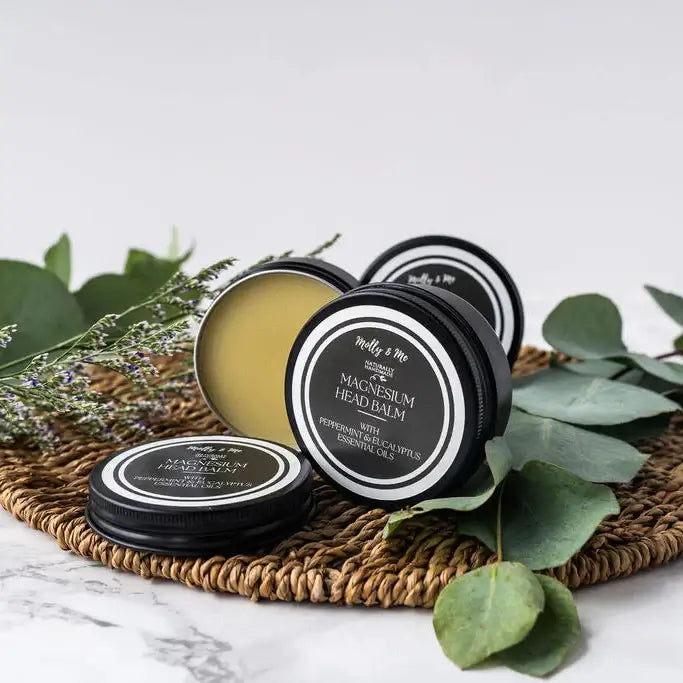 Jars of magnesium head balm on a woven mat with green leaves