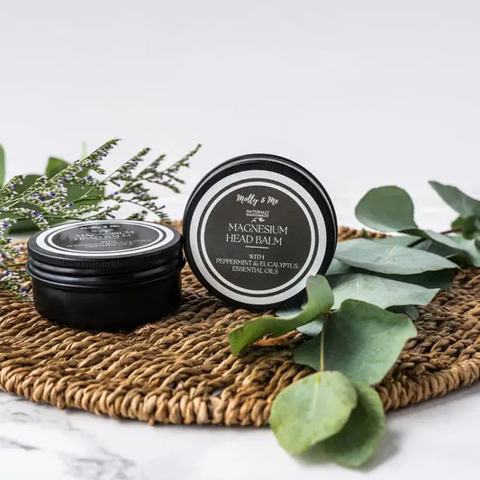 Two tins of magnesium head balm on a woven mat with green leaves.