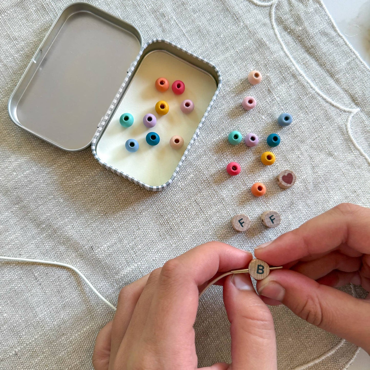 Colorful beads and letter beads on a textured surface with hands holding a letter bead.