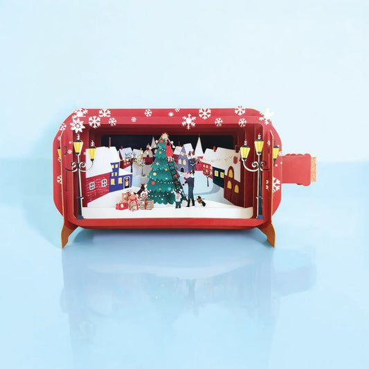 Pop-up Christmas card showing family decorating a Christmas tree in a snowy town centre with dogs, presents, and a festive 3D scene.