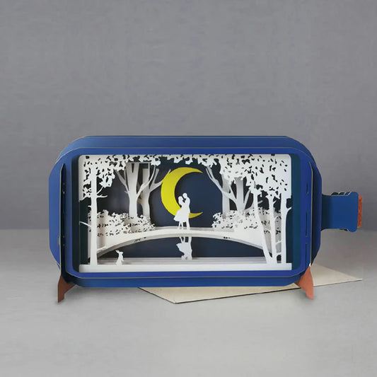Pop up card shaped like a bottle with a white laser cut  paper scene of a couple standing on a bridge among the trees under a yellow crescent moon. Small rabbit looking on