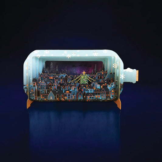 Pop up card shaped like a bottle with a night scene of a town with Christmas Lights and Christmas tree