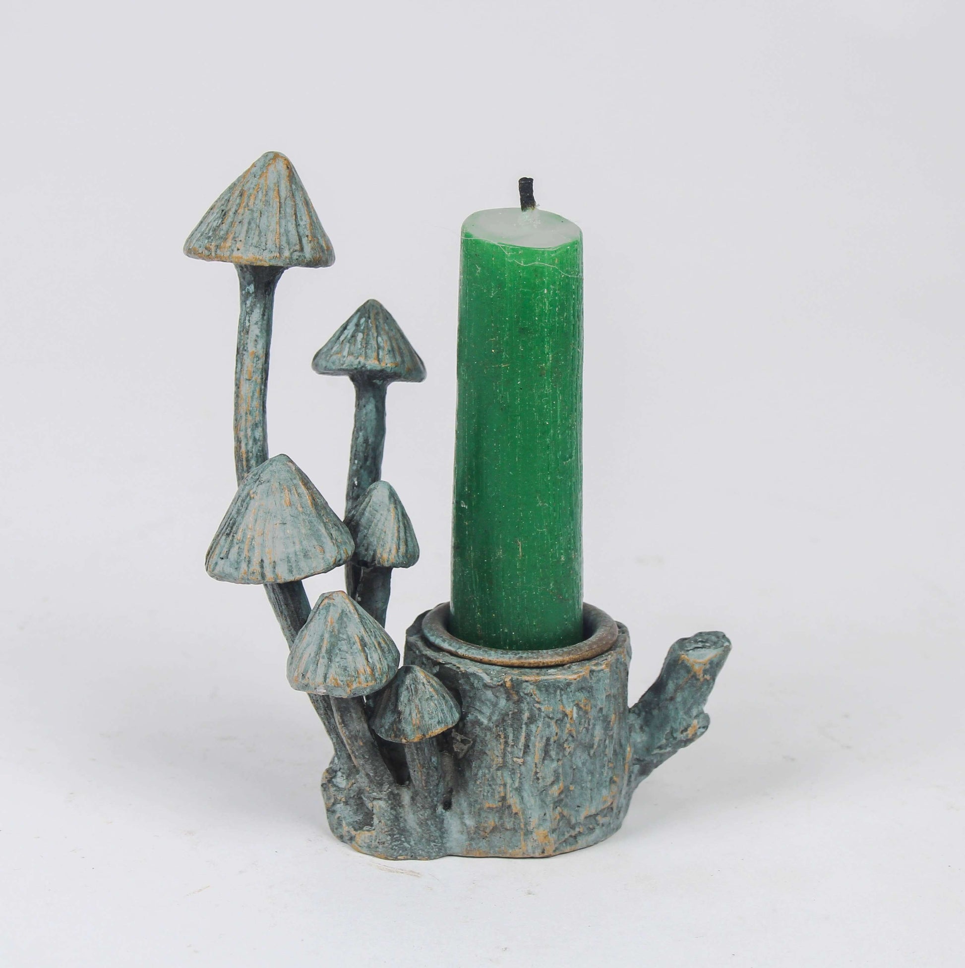 A verdigris-colored metal candle holder designed to resemble a tree stump with six mushrooms of varying heights surrounding it, set against a white background.