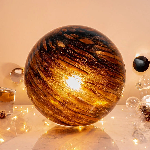 Decorative sphere lamp with a warm glow on a table with festive decorations.
