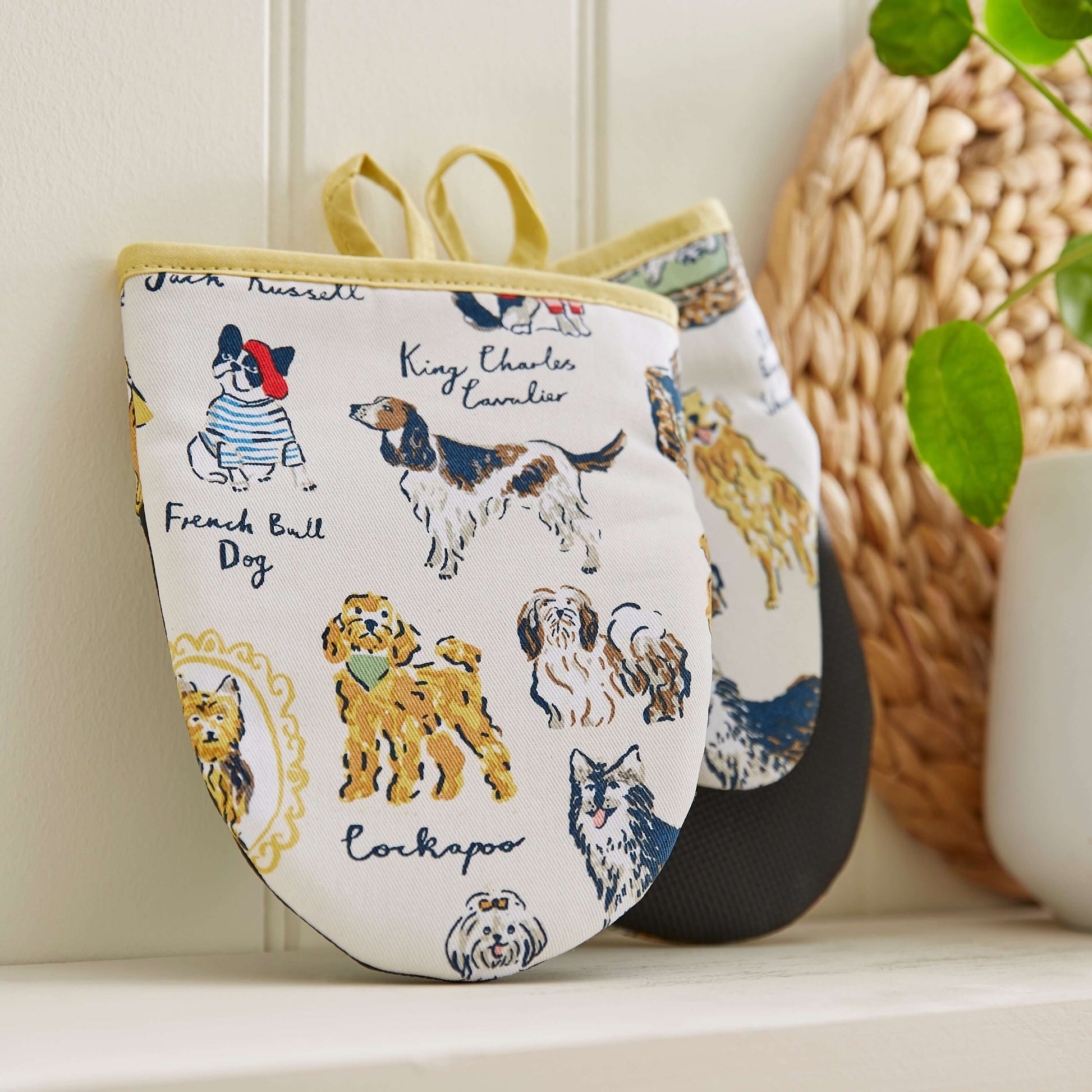 Pair of oven mitts with dog illustrations on a white surface.