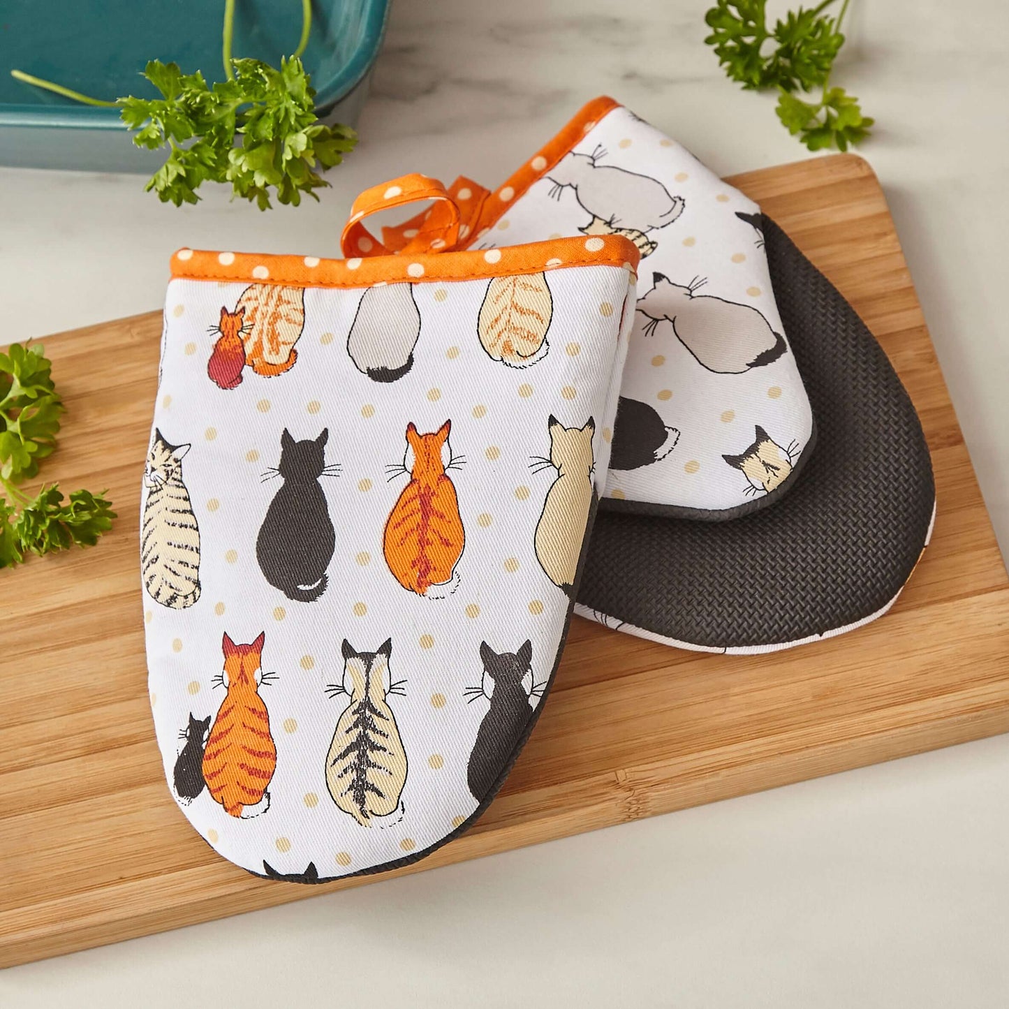 Pair of oven mitts with cat pattern on a wooden cutting board.