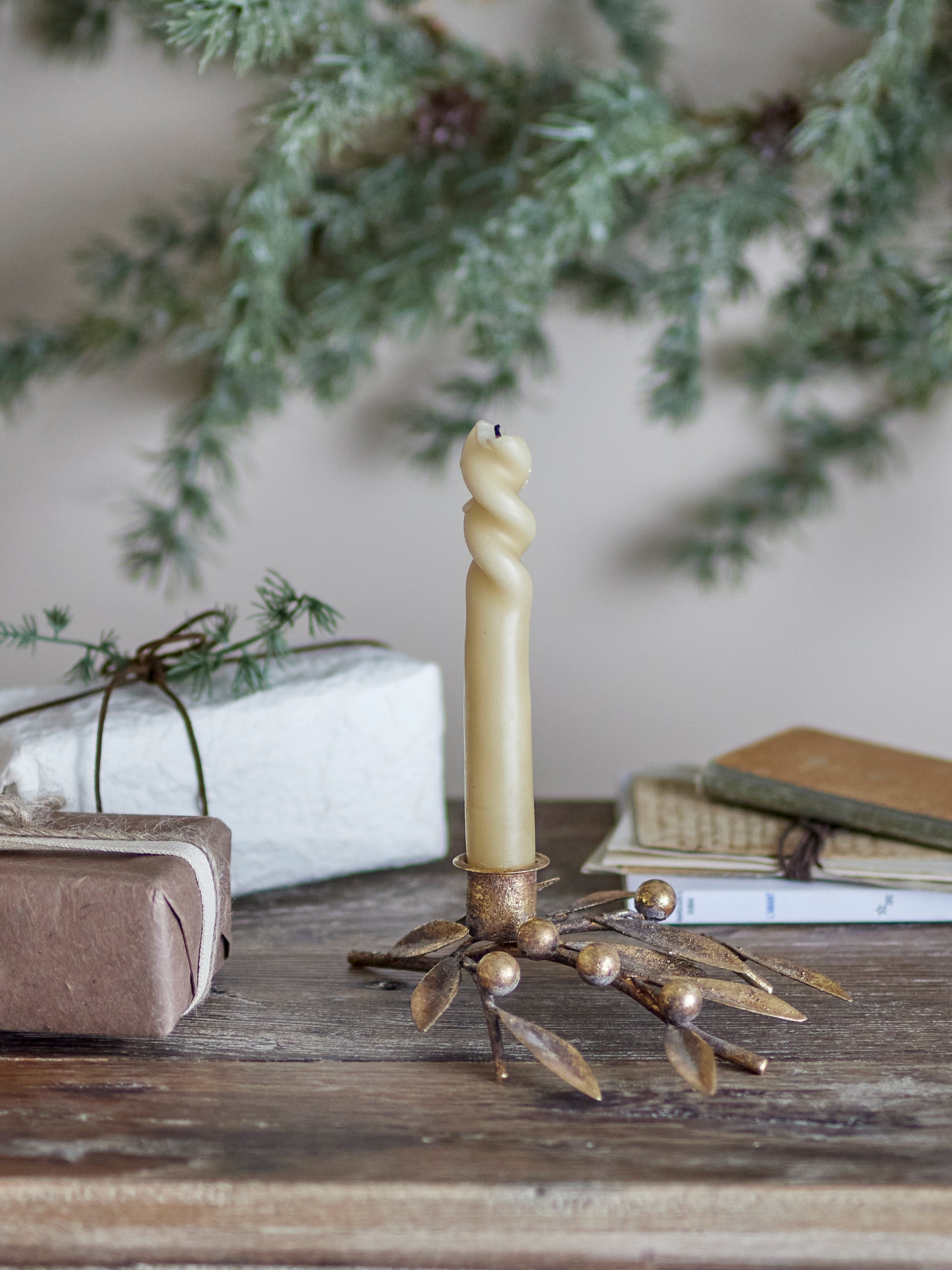 Decorative candle holder with a candle on a wooden surface with greenery in the background