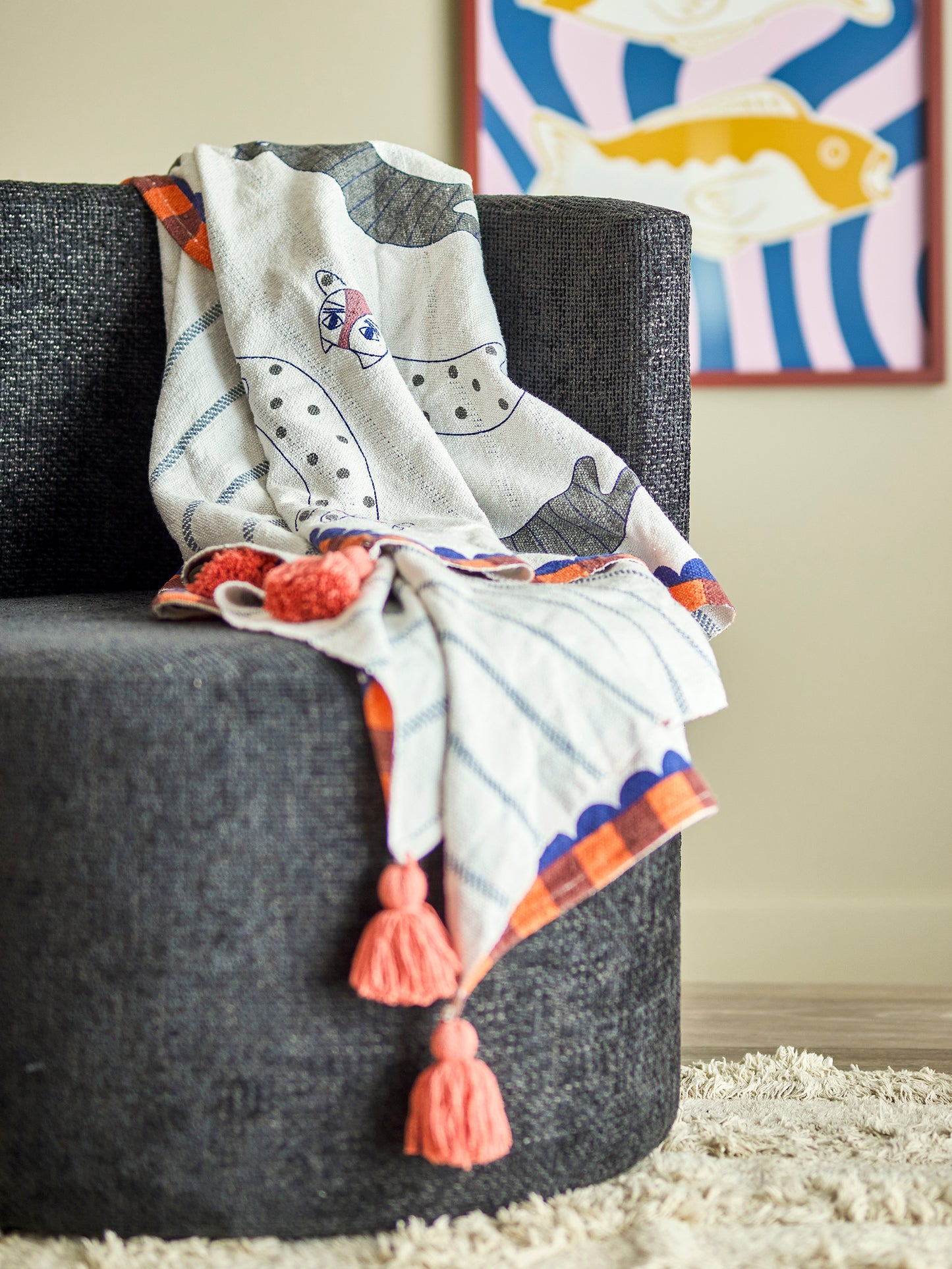 Decorative blanket with tassels draped over a dark gray chair, with a colorful abstract painting in the background.