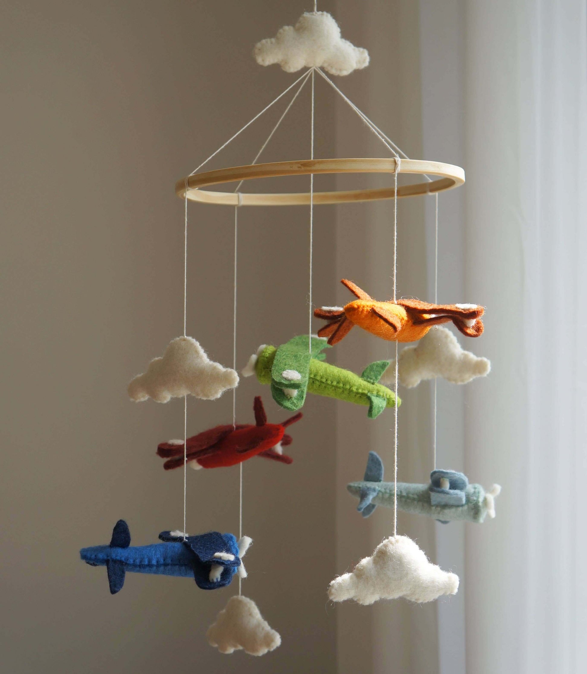 Handmade mobile featuring colorful airplane-shaped plush toys with clouds, hanging from a wooden ring.