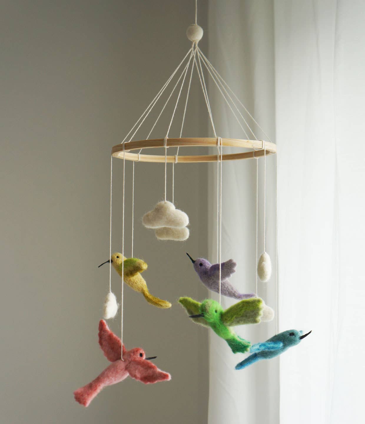 Colorful bird mobile hanging from a wooden ring against a neutral background