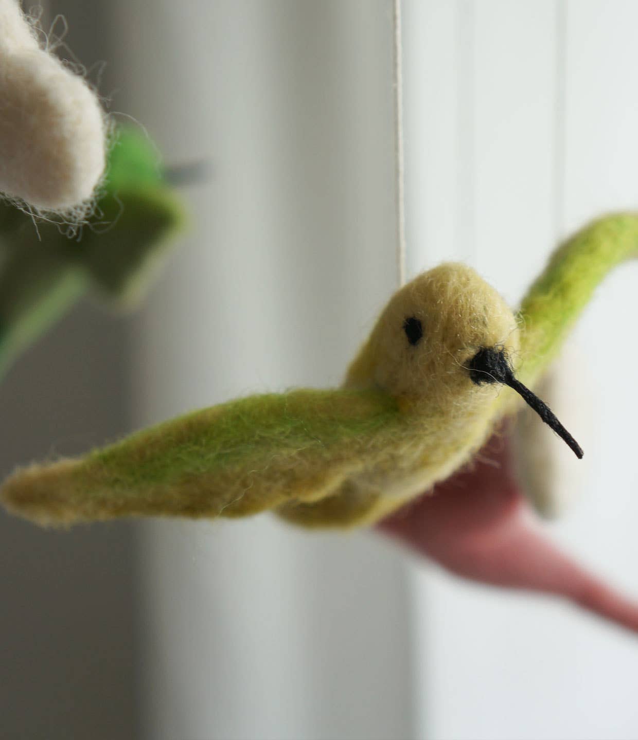 Felted yellow bird toy held by a hand with a blurred background