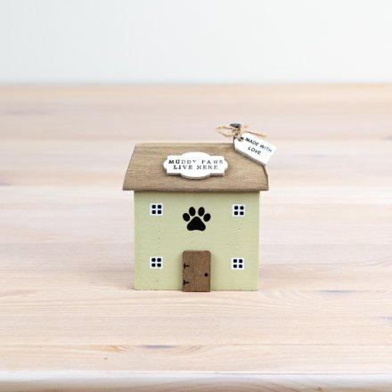 A small decorative house-shaped pet memorial or keepsake box with a pale green body, brown roof and door, black paw print on the front, and two hanging tags reading 'Muddy Paws Live Here' and 'Made with Love'.