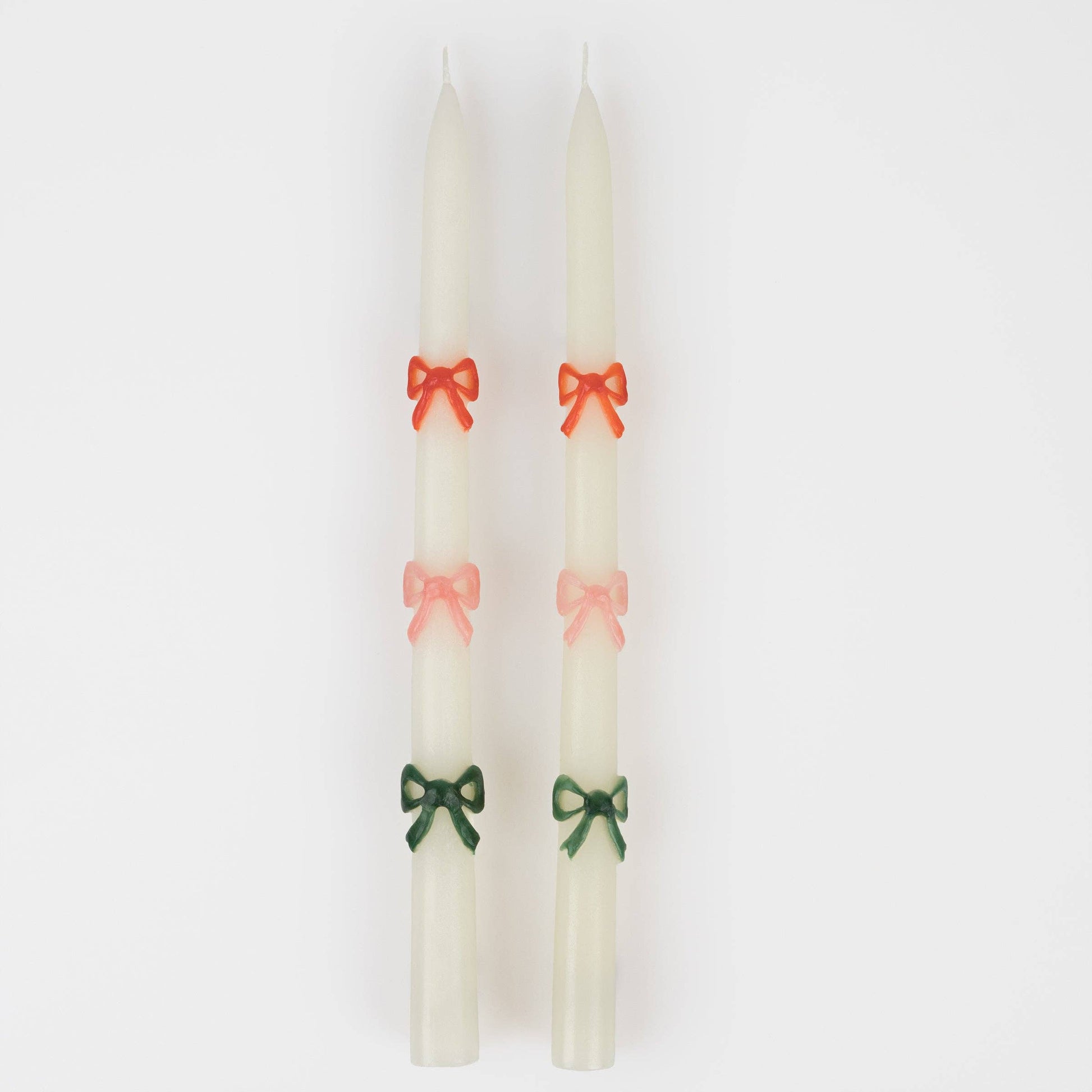 Two white candles with colorful bows on a white background