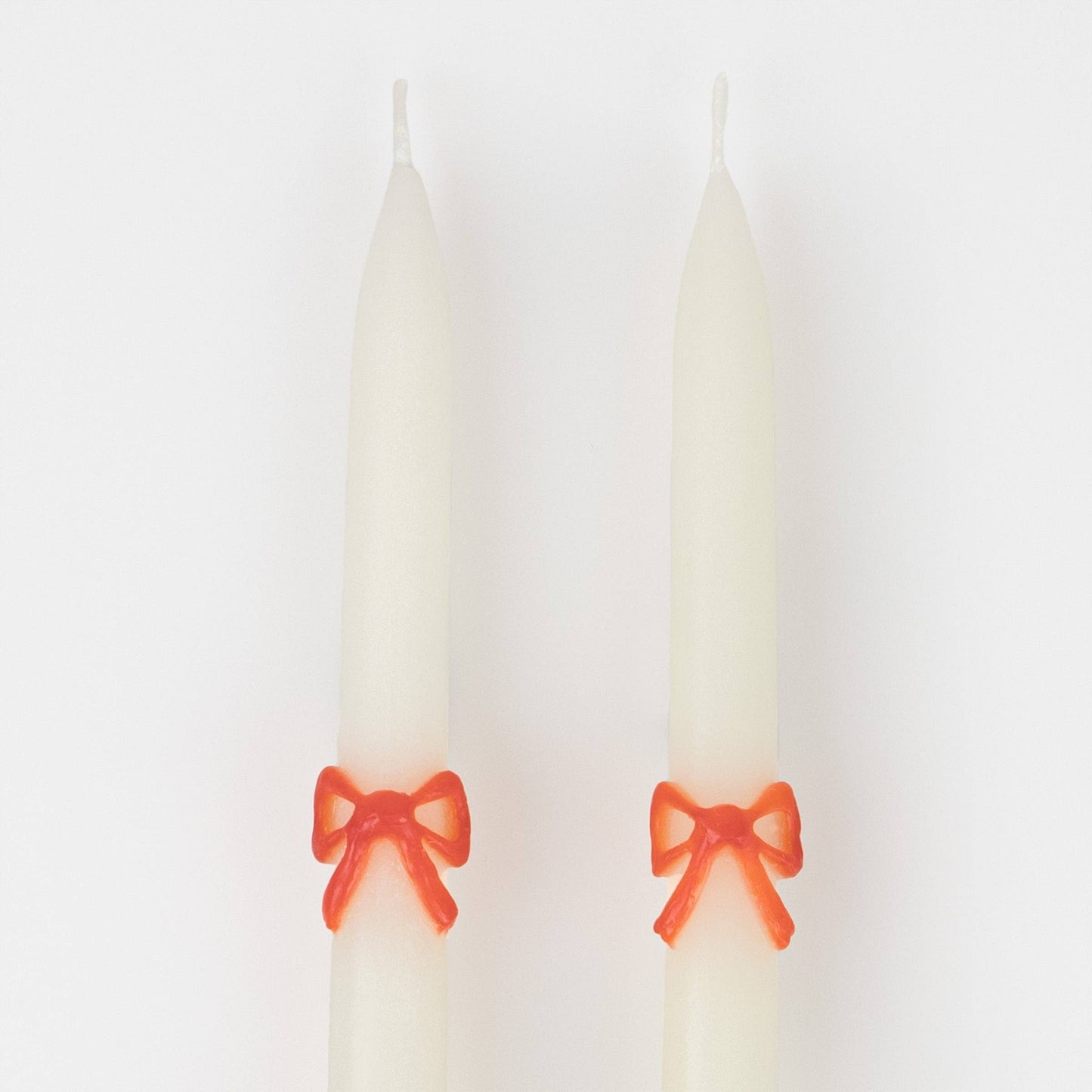 Two white candles with red bows on a white background