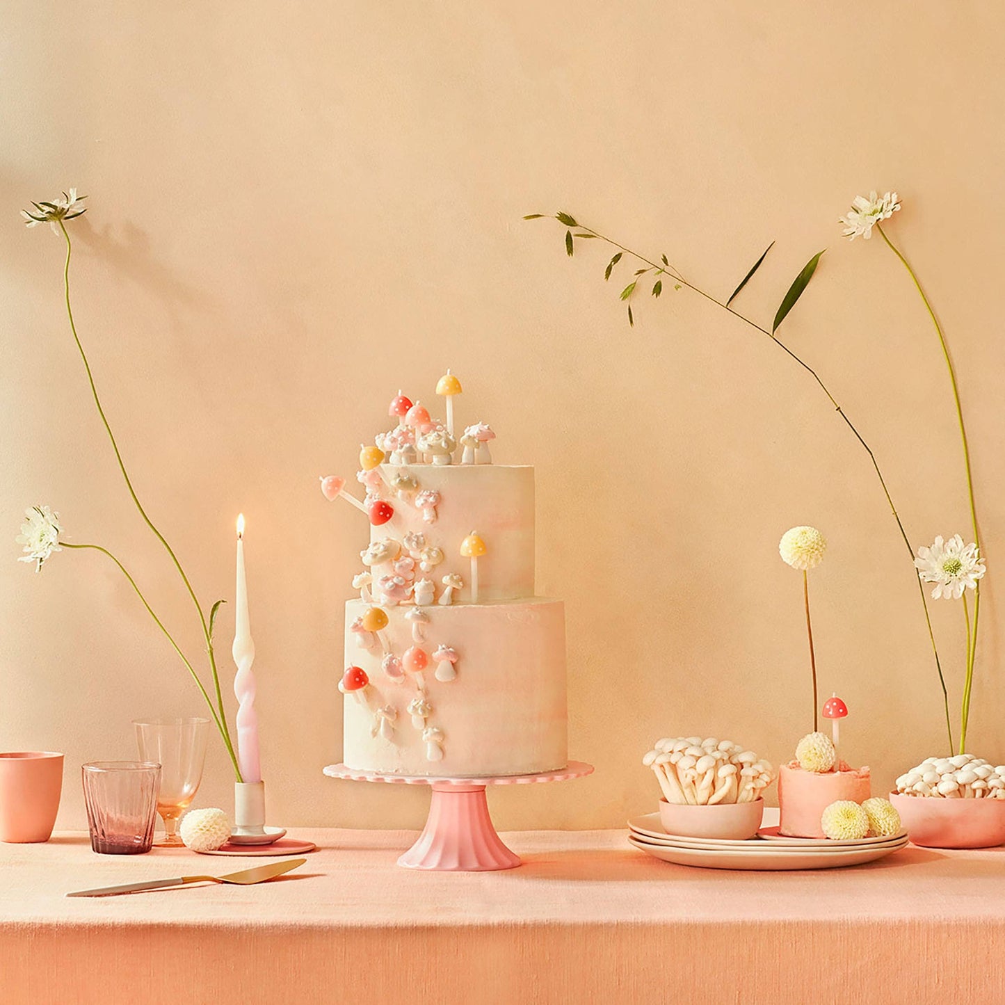 Decorative cake with small desserts on a pink stand against a peach-colored wall.