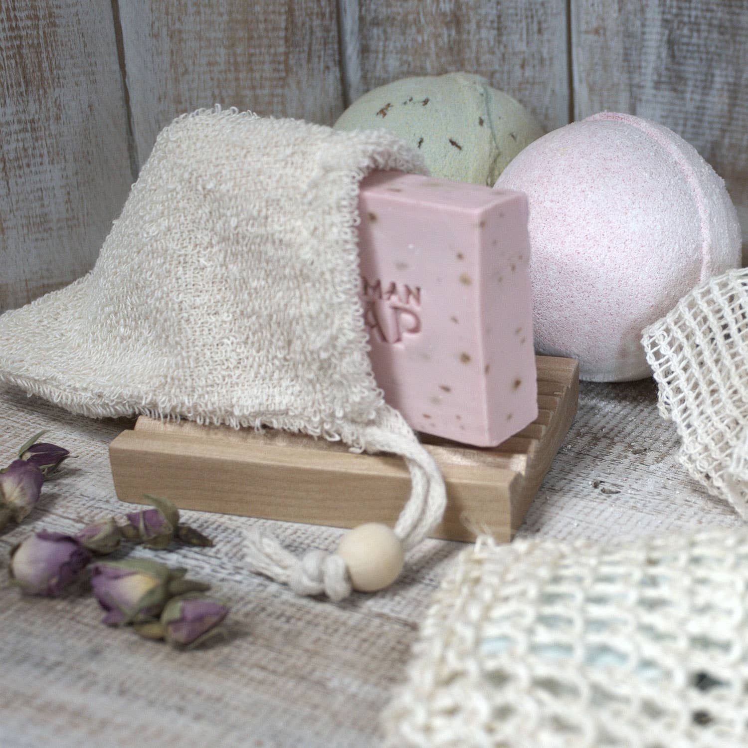 Bath products including a loofah, soap bar, and bath bomb on a wooden stand with a rustic background.