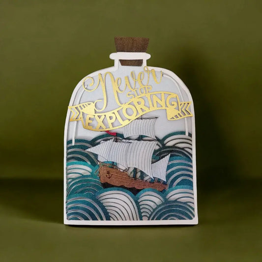 A decorative bottle-shaped greeting card featuring a white ship sailing between blue and teal waves, with gold foil text reading 'Never Give Up EXPLORING' and a brown cork stopper at the top, shown against an olive green background.