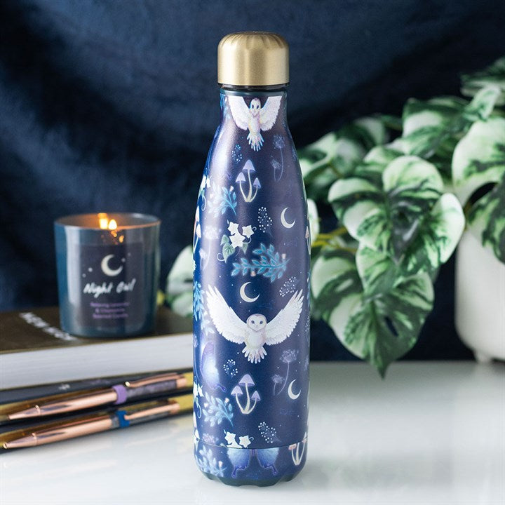 Blue water bottle with owl design on a surface with a candle and plants in the background