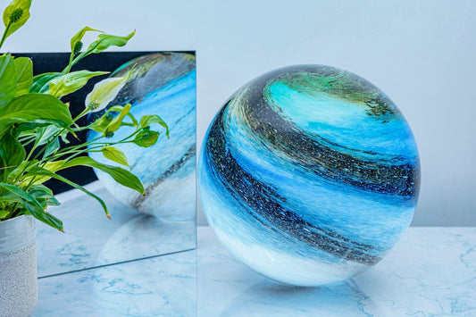Glass orb light with blue and white gradient on a light surface next to a plant