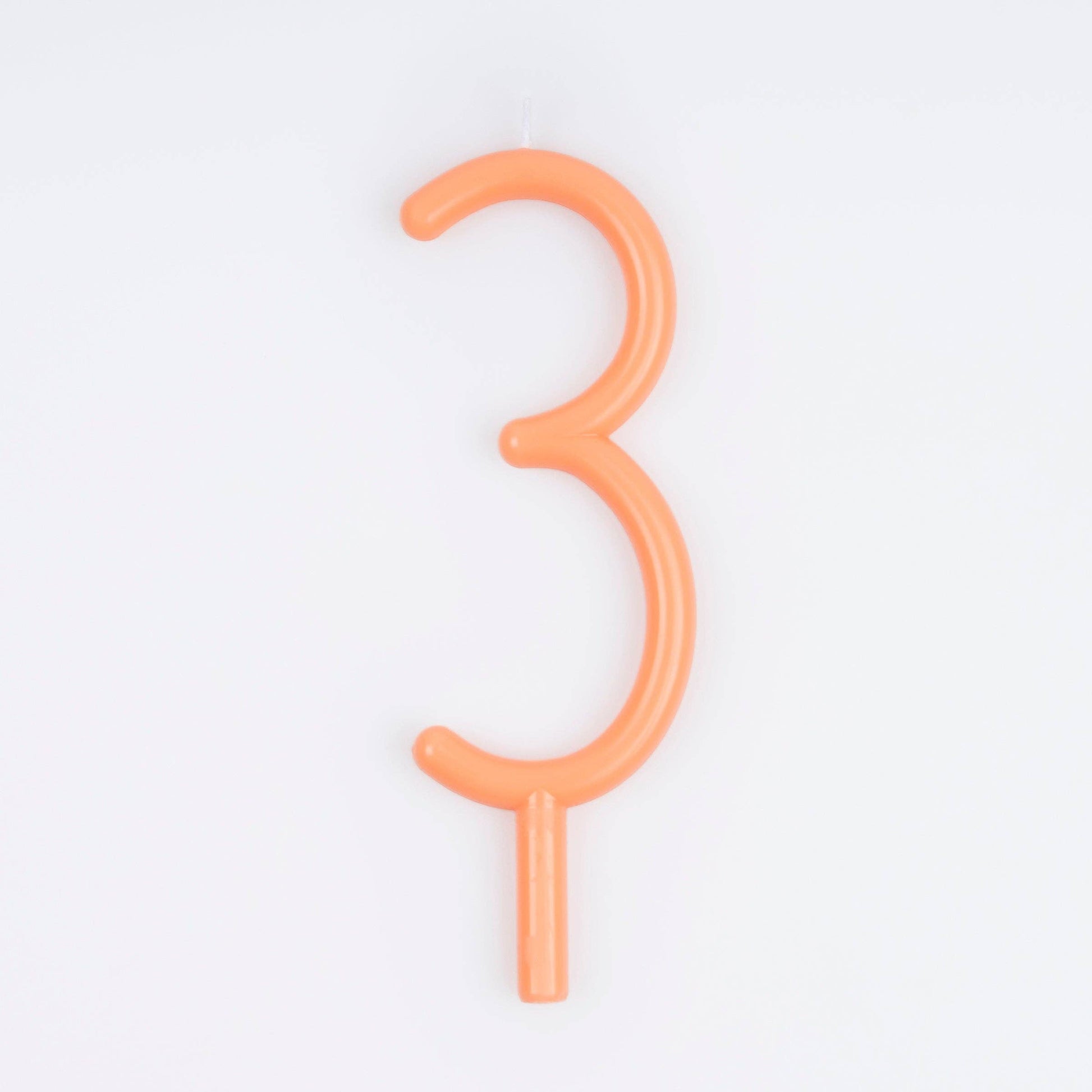 An orange wax number 3 birthday candle on a white background.