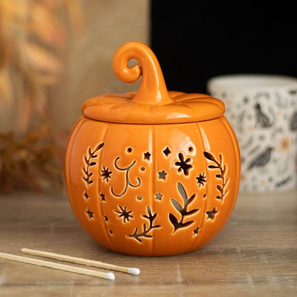 Ceramic pumpkin-shaped lantern with decorative cutouts on a wooden surface.