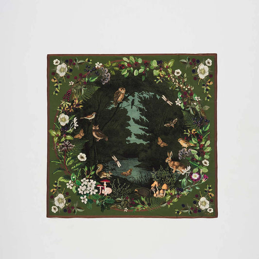 A square silk blend scarf featuring a detailed woodland scene with owls, rabbits, birds, butterflies, and a river, framed by a border of flowers and foliage on a light gray background.