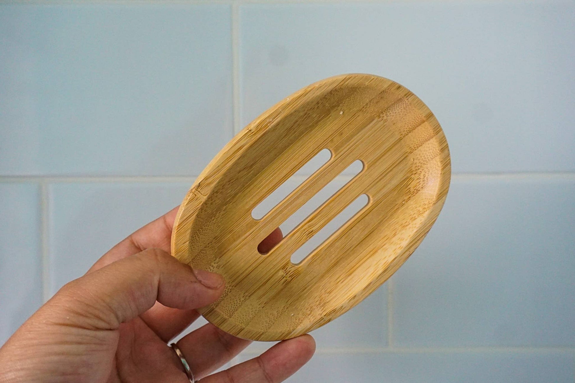 Hand holding a wooden soap dish against a tiled wall background
