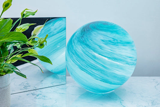 Turquoise glass sphere lamp on a marble surface with a plant in the background