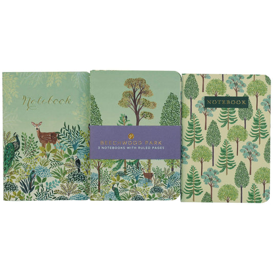 A set of three illustrated notebooks displayed side-by-side against a white background. The left notebook features a sage green cover with a deer and foliage; the middle notebook has a purple paper band label; the right notebook has a green and beige tree pattern.