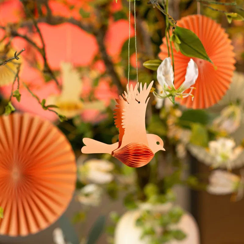 Decorative paper bird hanging among orange paper fans and green leaves