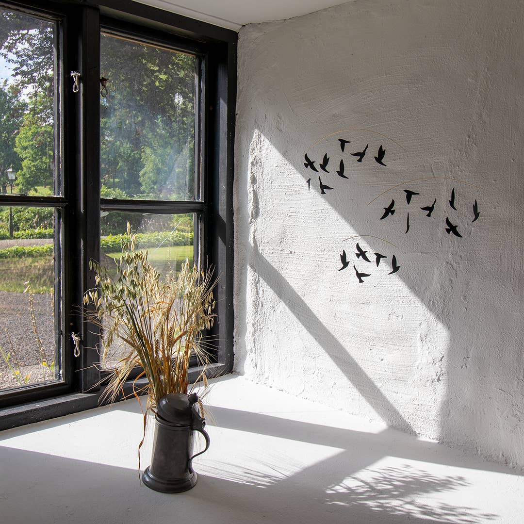 Room with a window, vase of dried plants, and wall with bird decals.