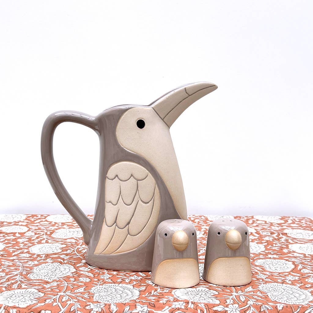 Ceramic bird-shaped pitcher and two small bird figures on a patterned tablecloth.