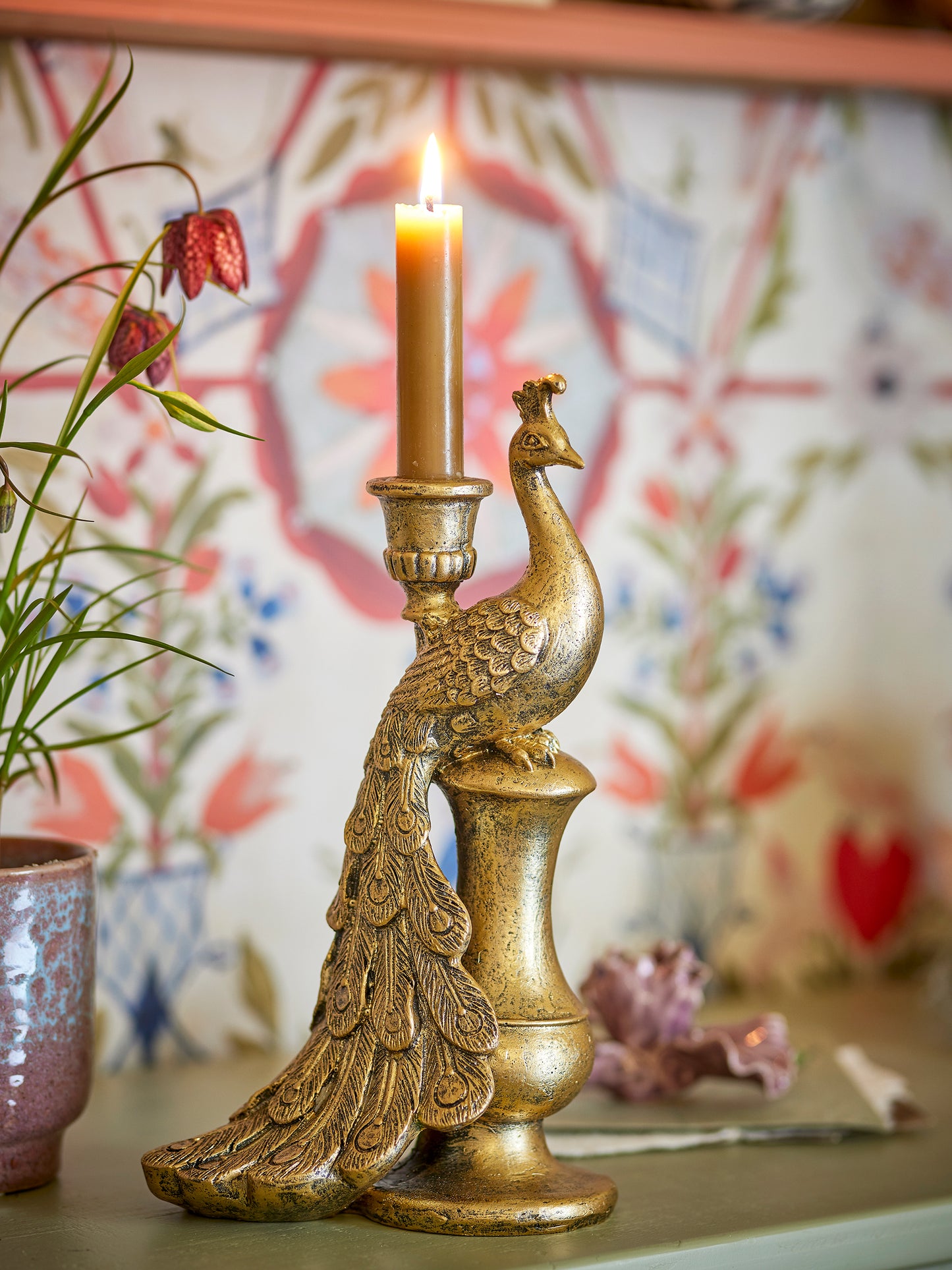 Gold peacock-shaped candle holder with a lit candle against a decorative background