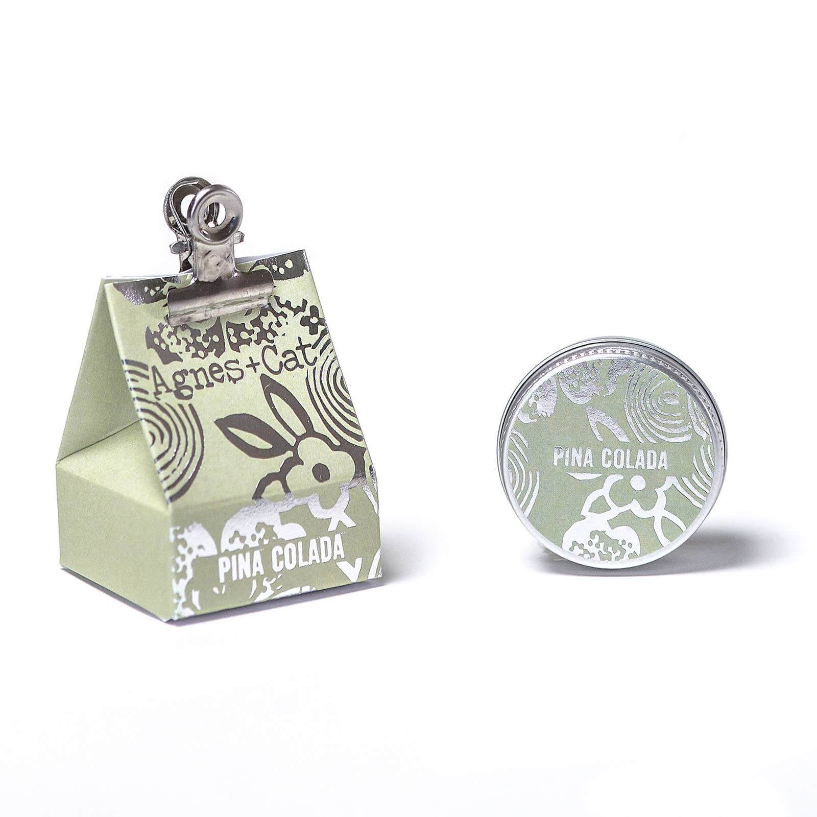 Image of lip balm tin in light green with packaging with silver decoration and 'Agnes + Cat' 