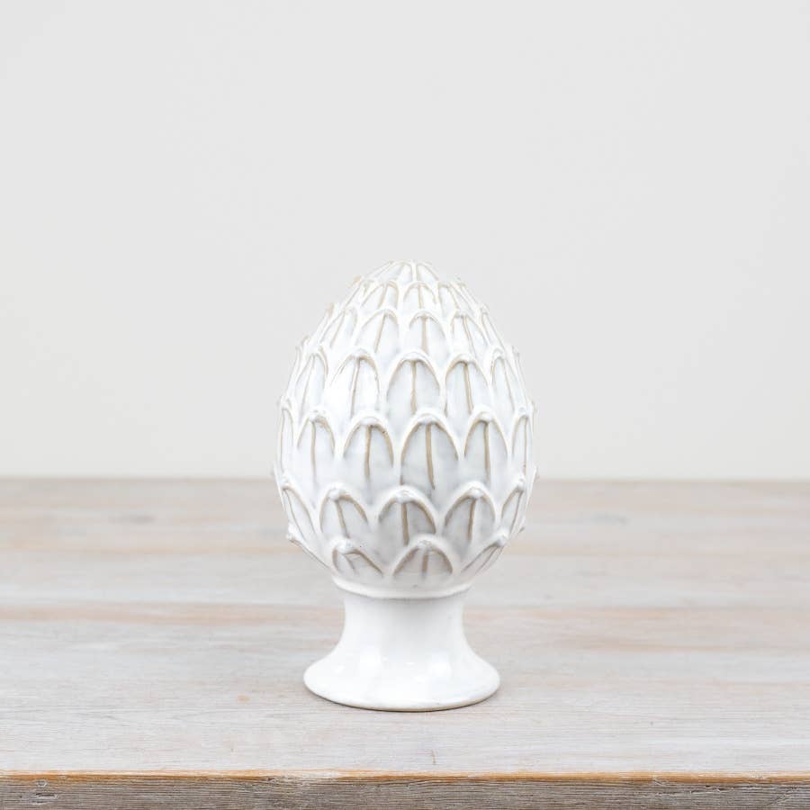 White ceramic artichoke-shaped object on a wooden surface with a light gray background