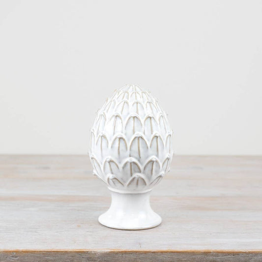 White ceramic artichoke-shaped object on a wooden surface with a light gray background