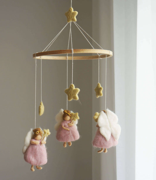 A decorative mobile featuring three pink fairies in dresses with magic wands, surrounded by yellow stars, hanging against a neutral background.