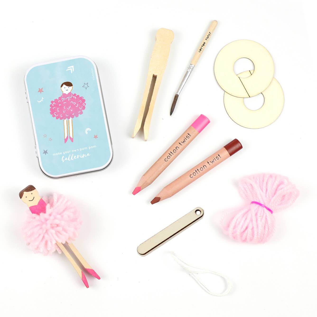 A collection of crafting materials for making a pom pom ballerina peg doll, including a wooden peg doll, wool, pom pom makers, watercolour pencils, a wooden needle, glue, a mini paintbrush, and a keepsake tin with a fairy design.