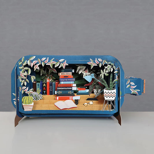 Pop up card shaped like a bottle with a scene of books and plants. Well done You've passed congratulations, written on the binding of the books