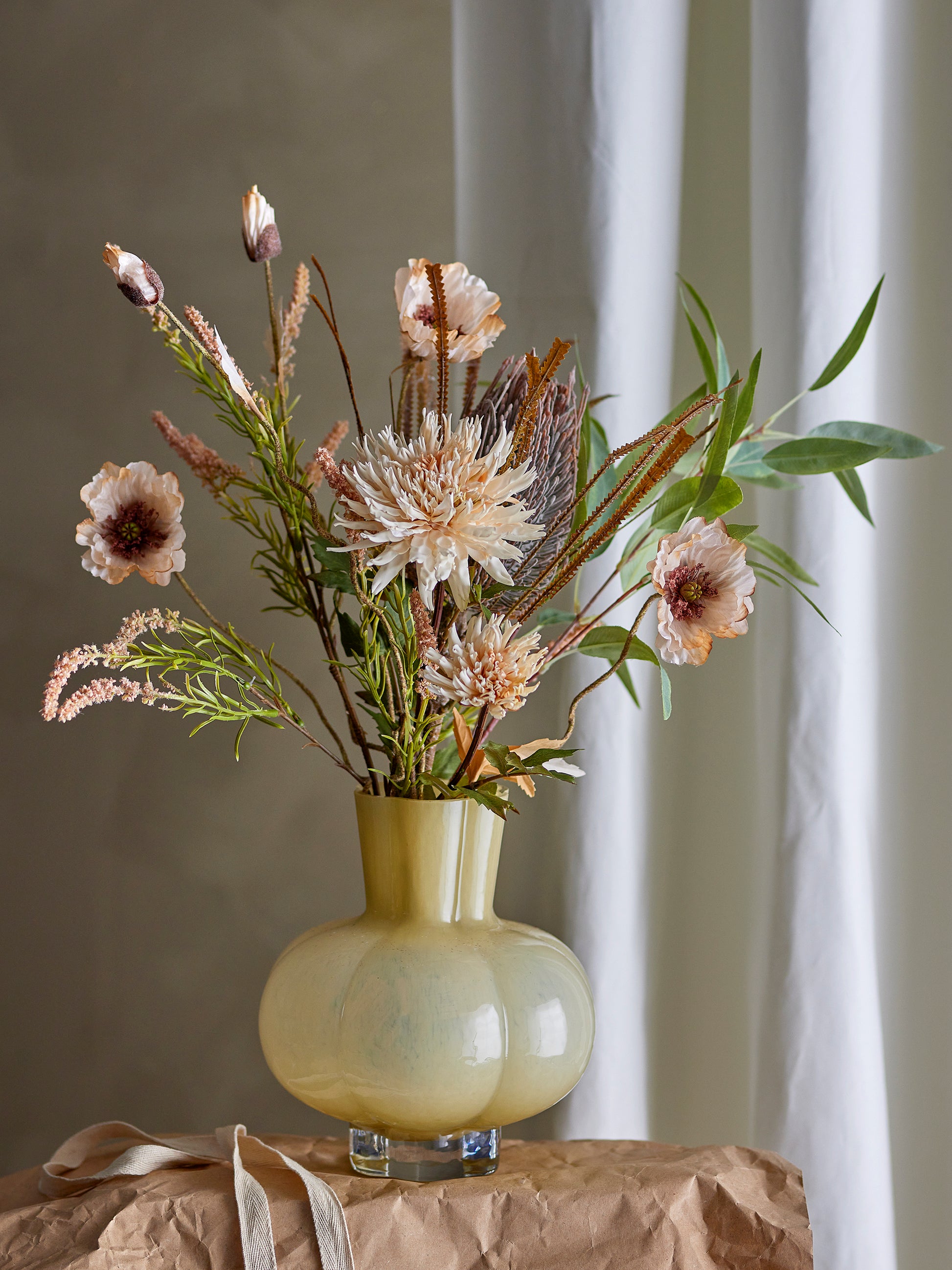 Decorative floral arrangement in a yellow vase on a surface with a neutral background