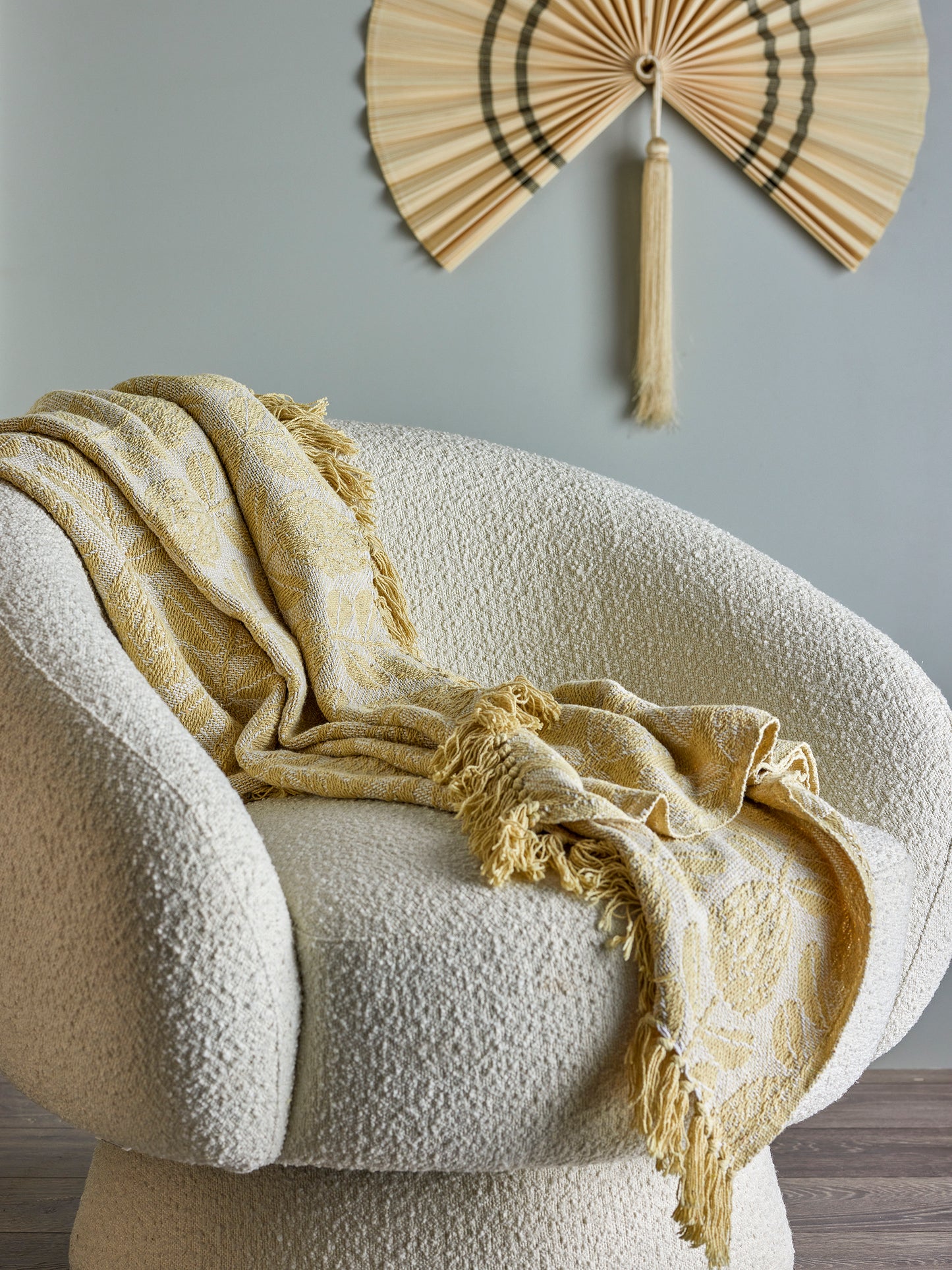 Beige blanket draped over a textured chair with a decorative fan on the wall.