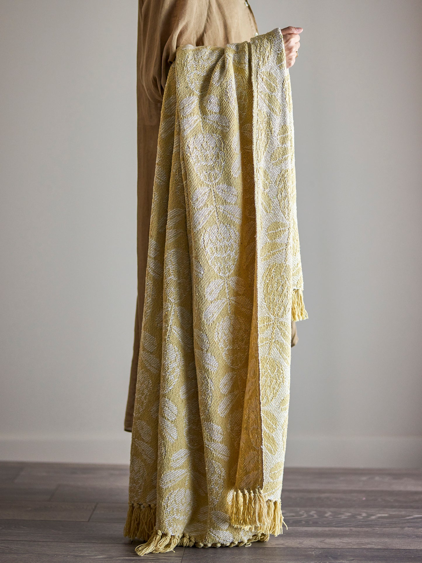 Person holding a long, patterned yellow and white throw against a plain background